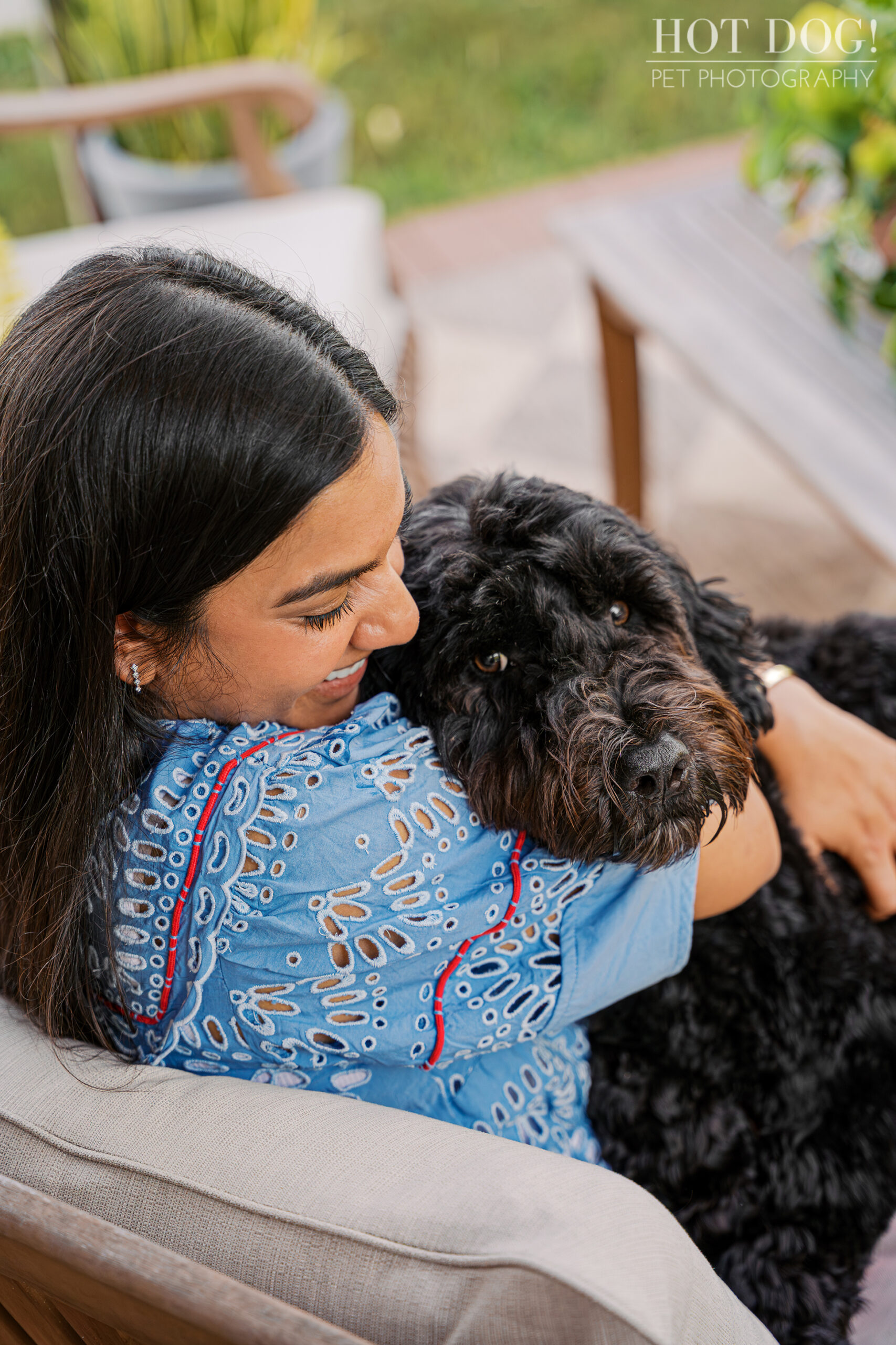 Selavi hugs Banjo close while he looks toward the camera, resting comfortably in her arms on the outdoor sofa.