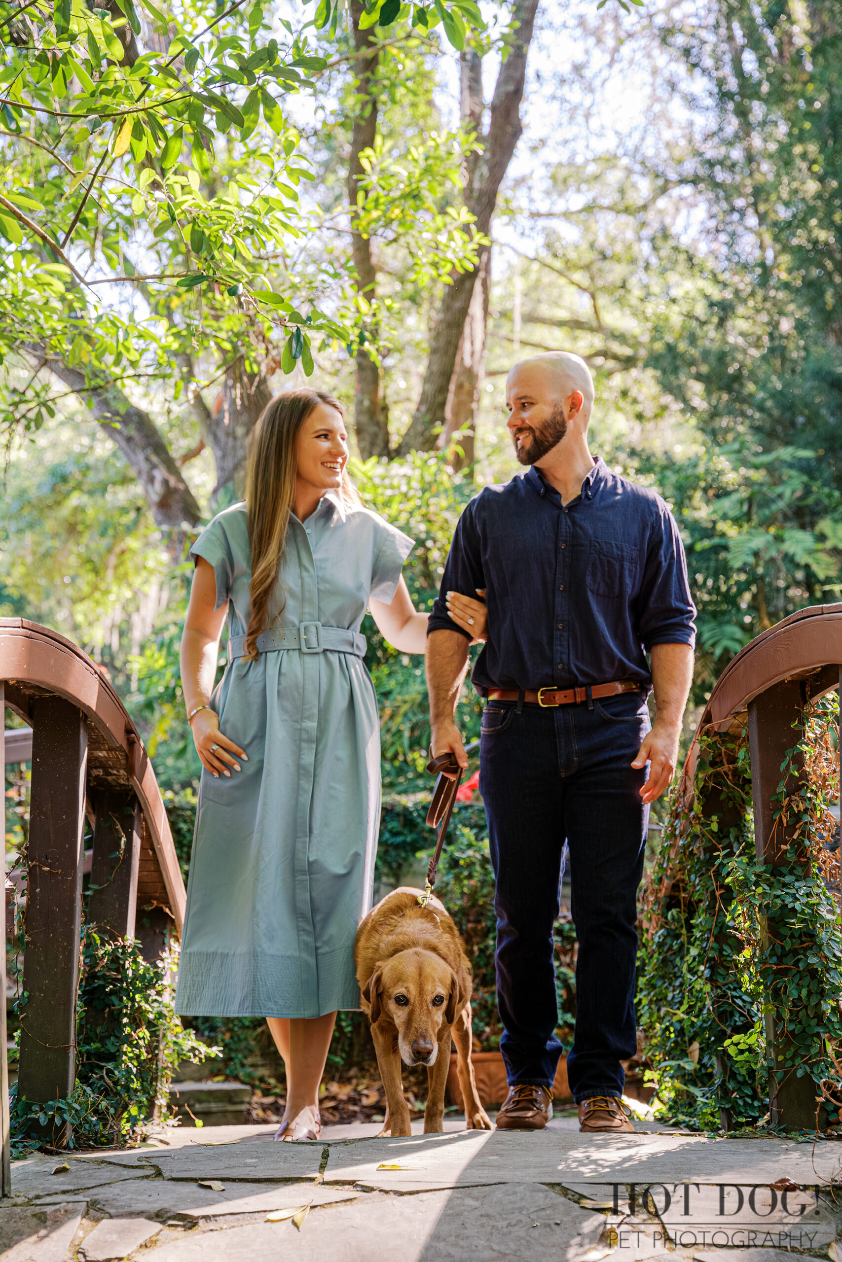 Chloe and Bryson walk with their senior Labrador Retriever, Dixie, across a garden bridge at Kanapaha Botanical Gardens.