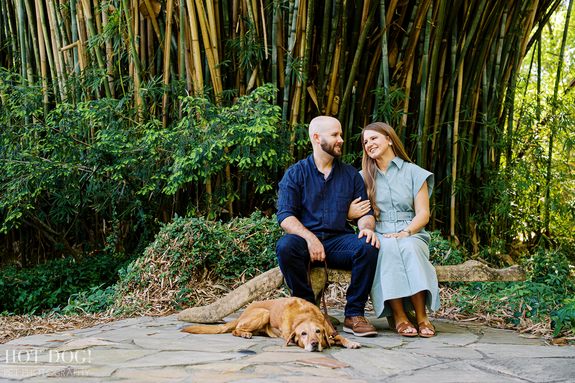 Chloe and Bryson sit together on a stone bench while Dixie relaxes at their feet during a pet photography session at Kanapaha Botanical Gardens.