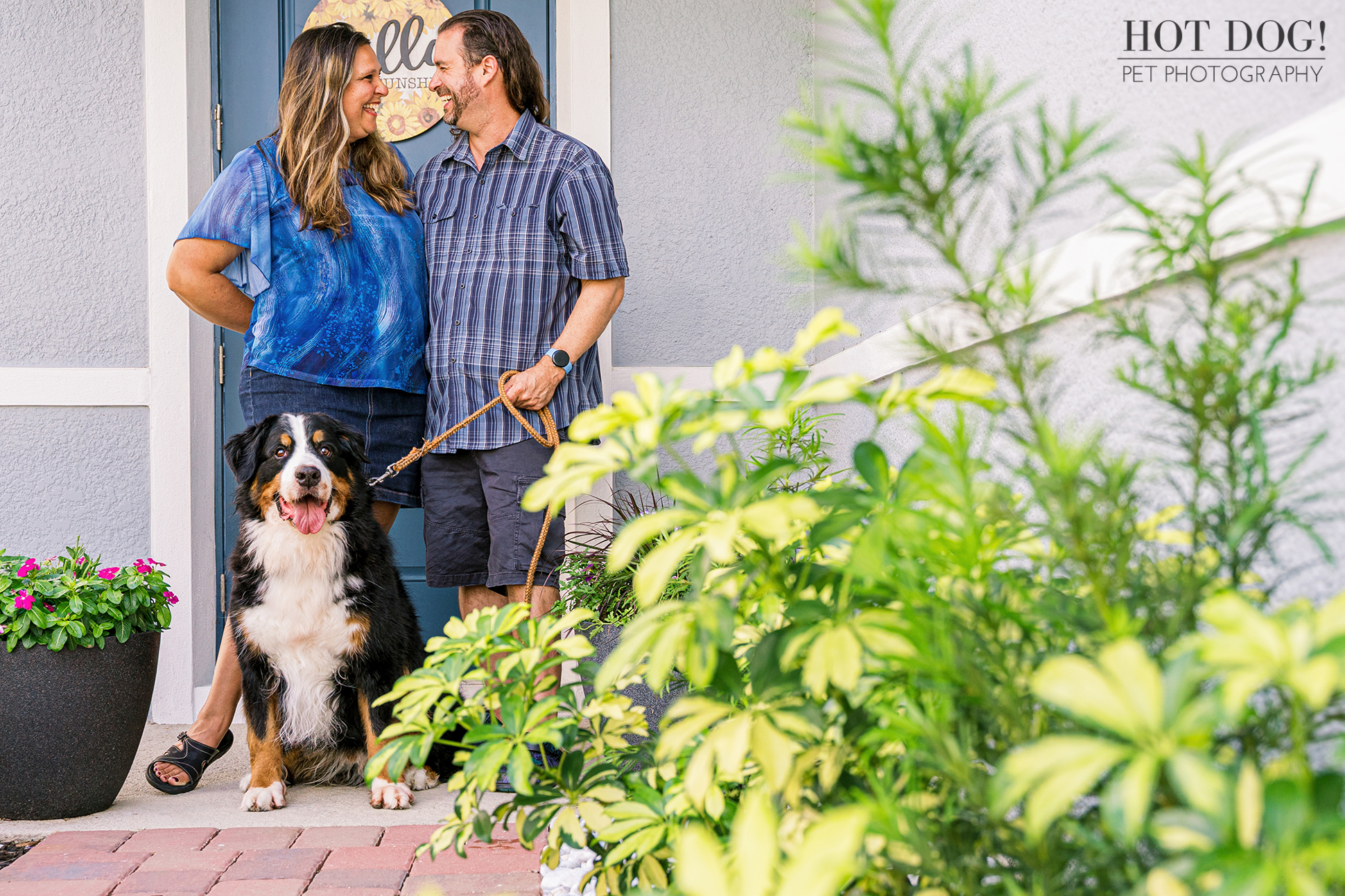 Helen and Jeremy smiling at each other with Flynn the Bernese Mountain Dog sitting at their front door.