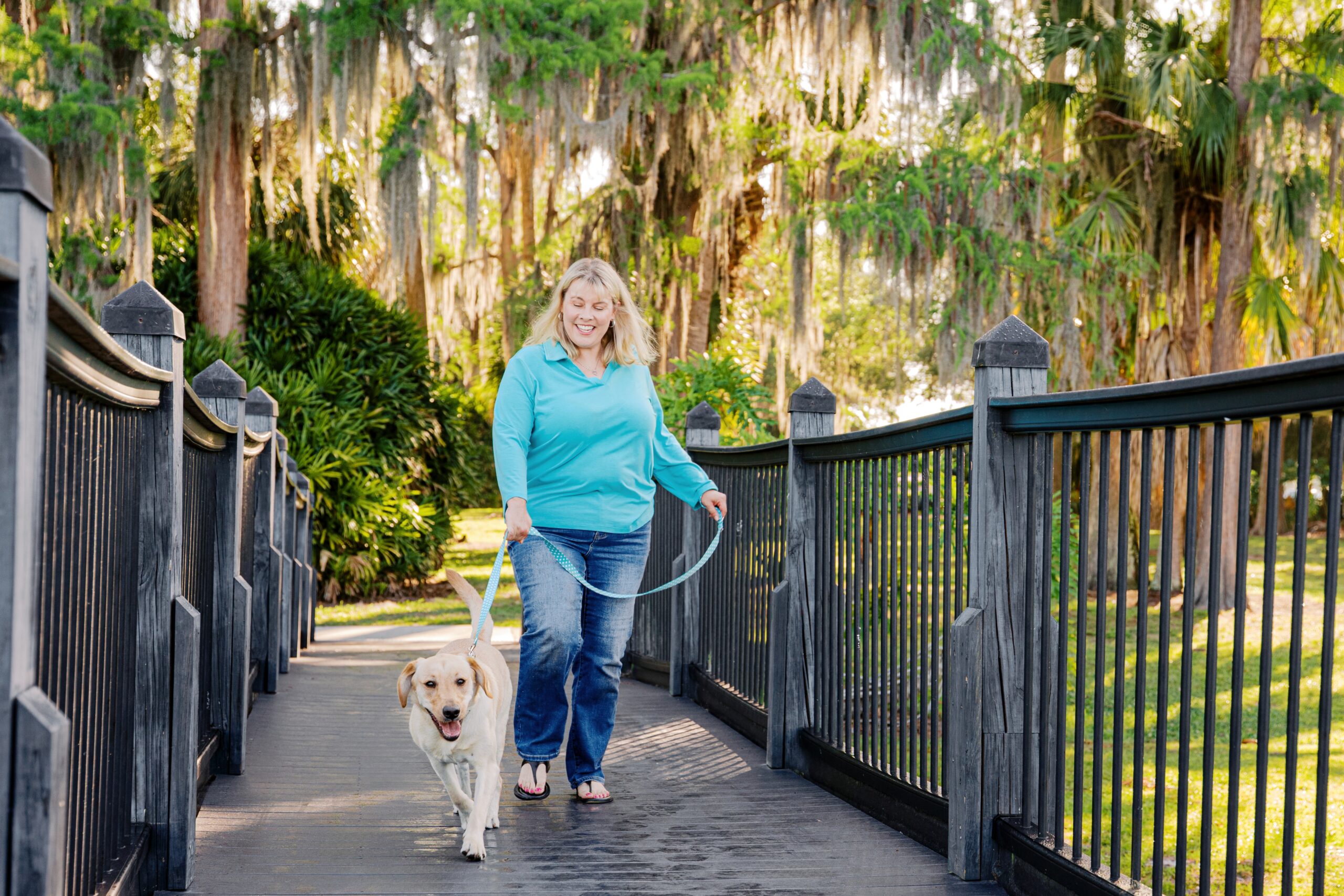 Woman walking with her yellow Labrador Retriever across a wooden bridge at Cypress Grove Park.