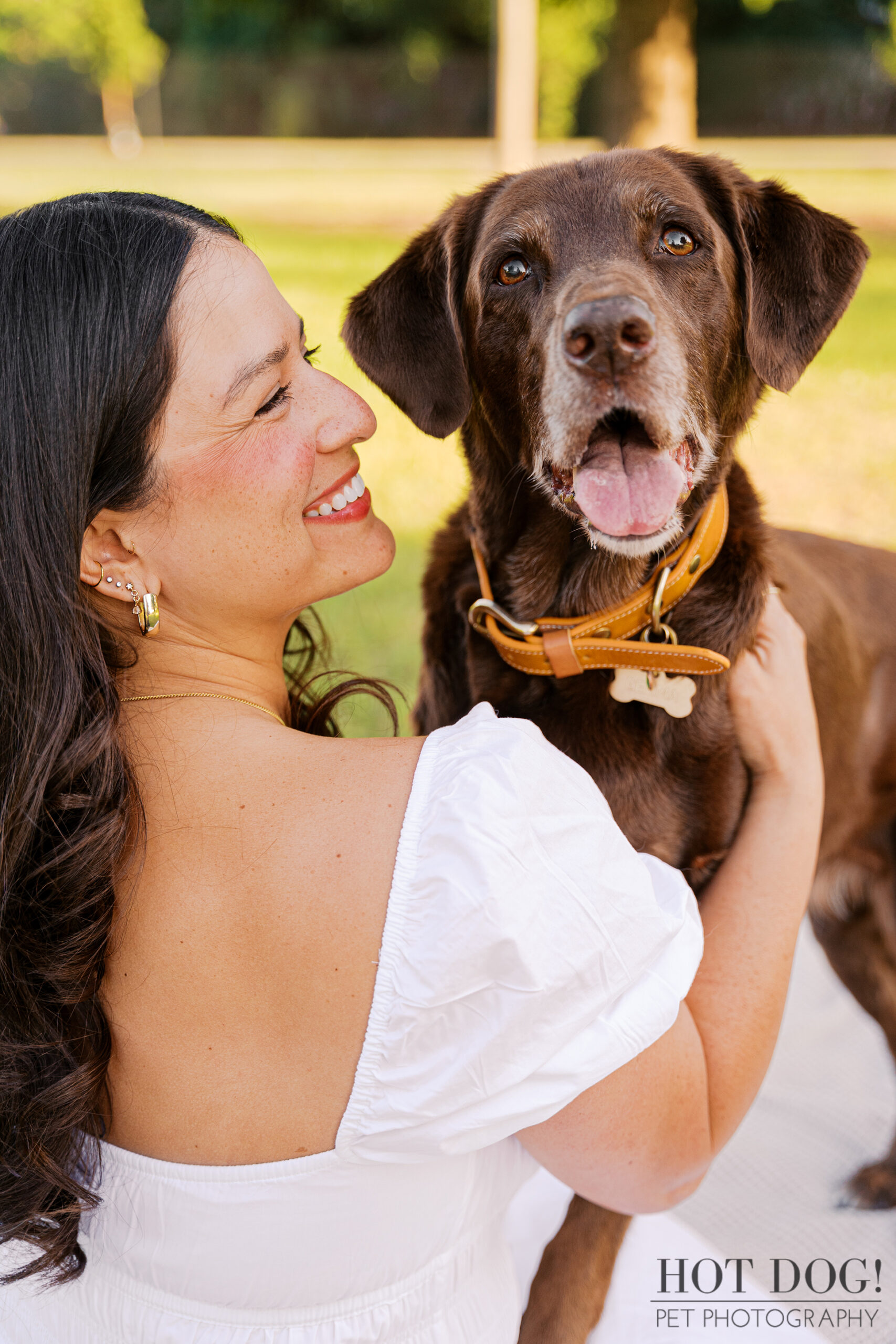 Anne smiles while holding Gemma, her senior brown Lab mix, during a heartfelt pet photography session at Lake Druid Park.