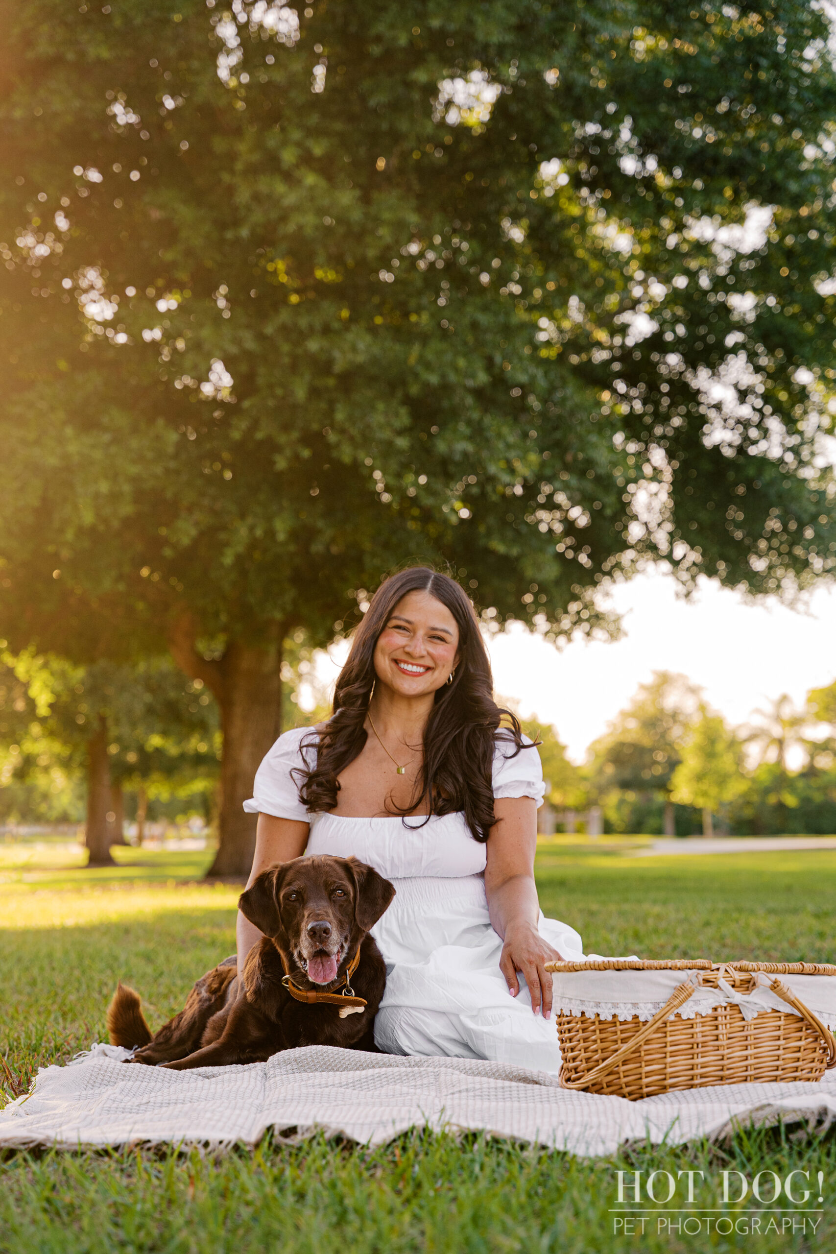 Anne and Gemma relax on a picnic blanket beneath a large oak tree during a golden-hour dog photography session at Lake Druid Park in Orlando.