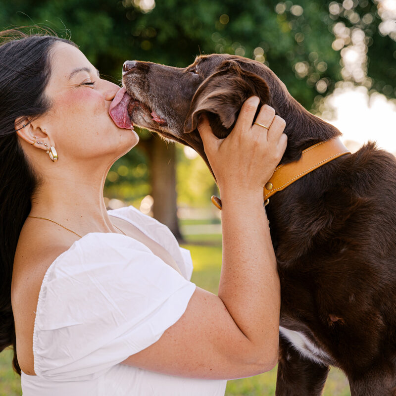 Gemma gives Anne a big kiss during their outdoor pet photography session, capturing the affectionate bond they share.
