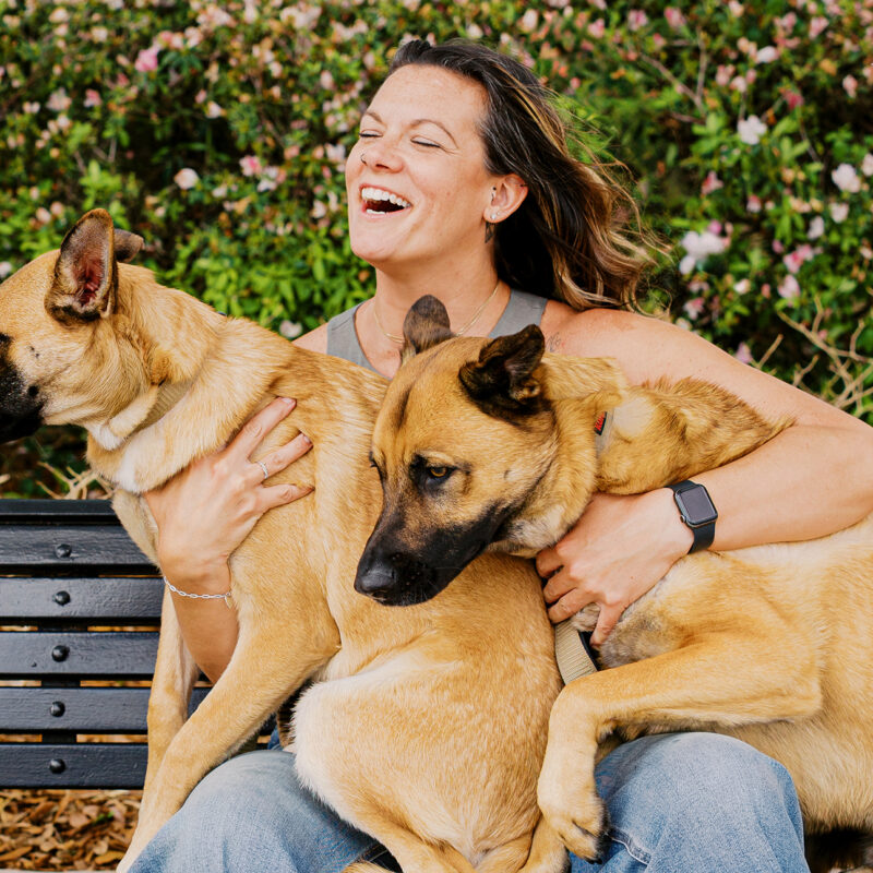 Krystle holding Maverick and Goose together on her lap on a park bench, capturing their affectionate bond during a Baldwin Park session.