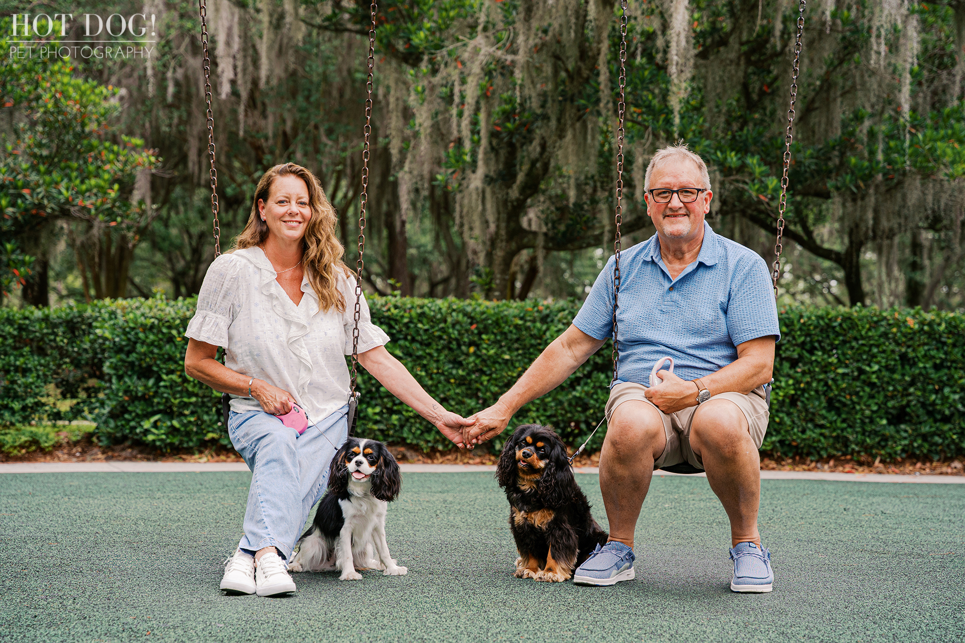 Tonia and James holding hands on swings with Cavalier King Charles Spaniels Jerzee and Jazmyn beside them during their Central Florida pet photography session.