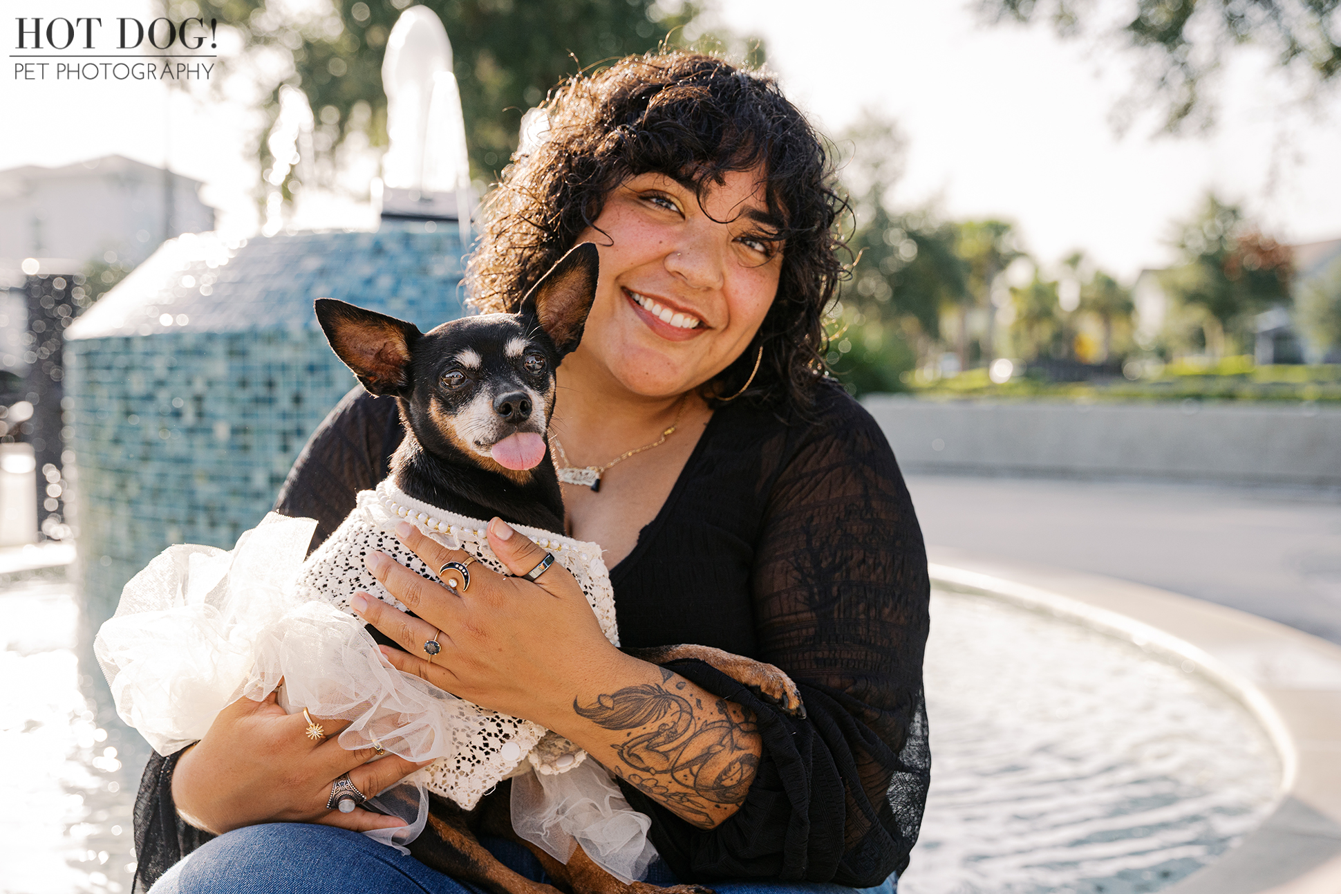 Gabriela holding Kiki the Miniature Pinscher in a white lace and tulle dress, sitting by a blue tile fountain in Lake Nona.