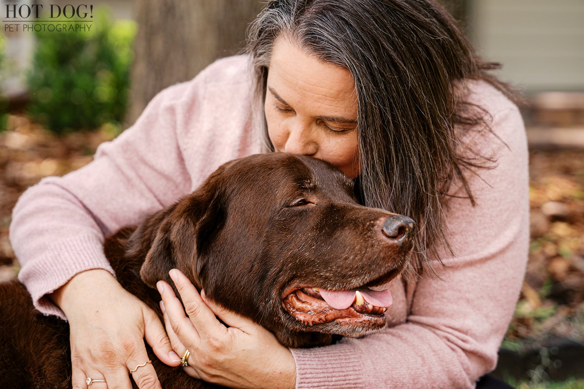 Jennifer embraces her beloved chocolate Labrador Retriever, Kona, and kisses his head during an intimate at-home senior dog photography session in Oviedo, Florida.