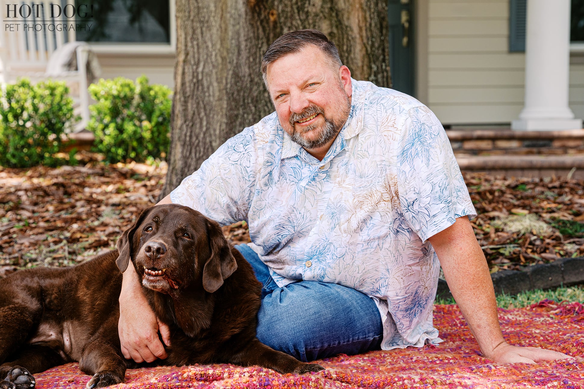 James smiles beside his beloved senior chocolate Lab, Kona, as they relax together on a colorful blanket in the family's front yard.