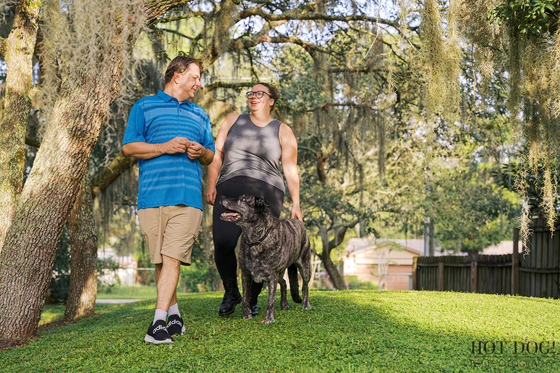 Lukasz and Natasha walking with Leah beneath mossy oak trees in their yard, smiling together.