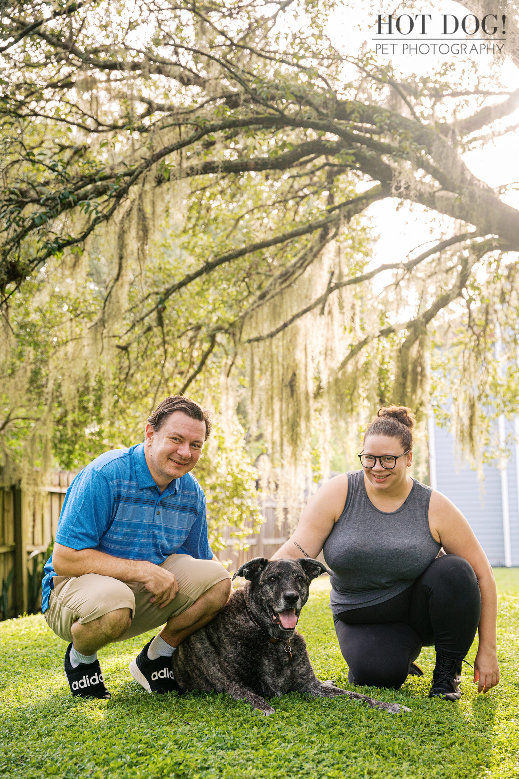 Lukasz and Natasha kneeling with Leah in the grass, smiling together in the sunlight.