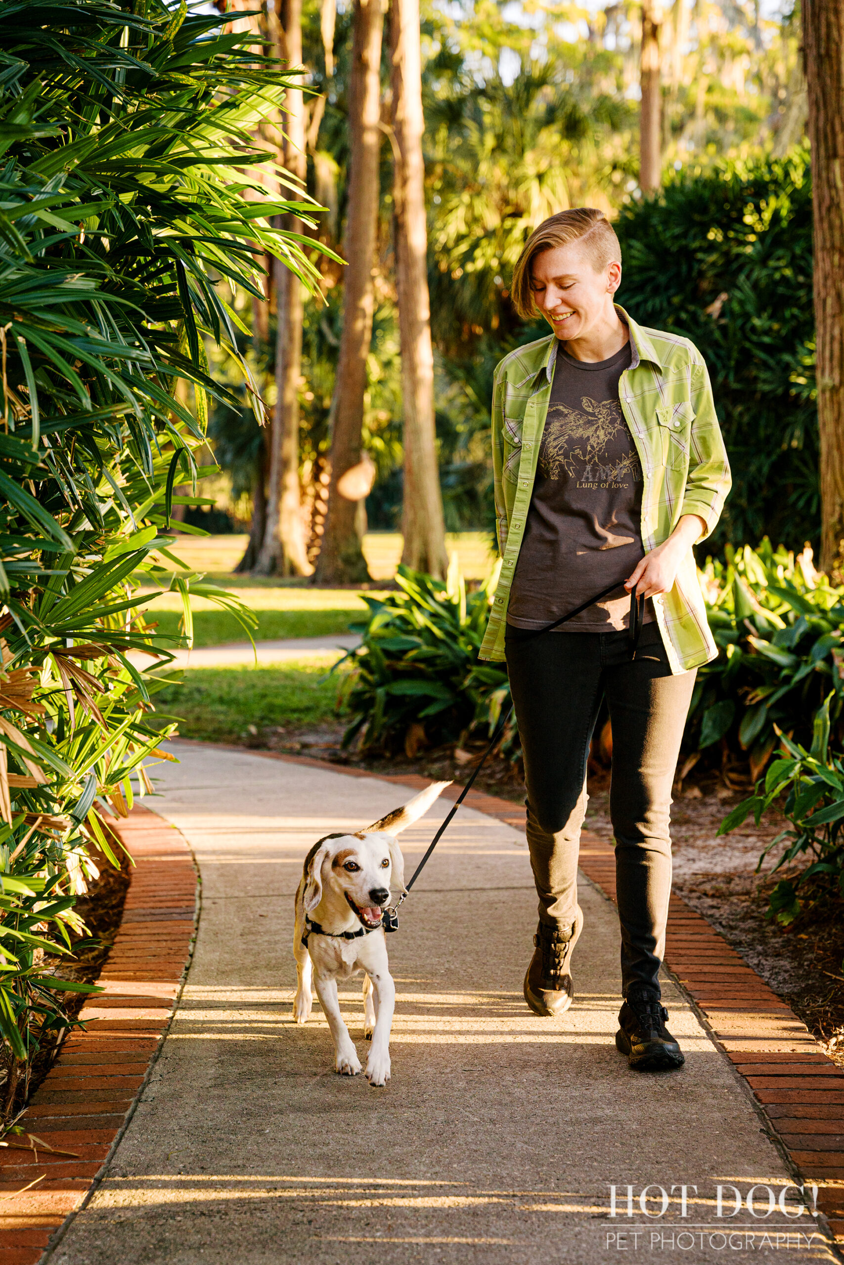 Melanie walking her tri-color beagle Leonard along a shaded park path surrounded by lush greenery.