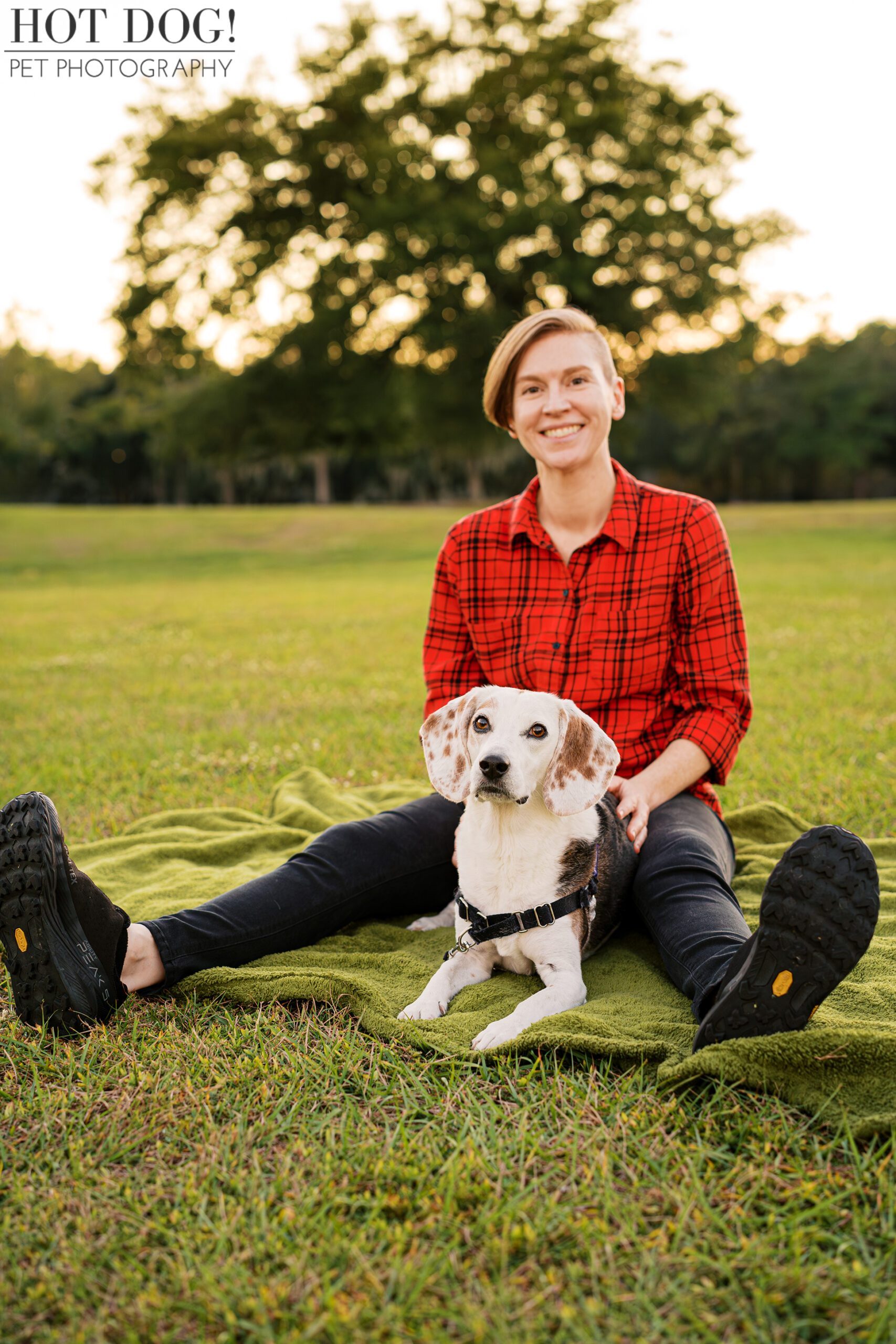 Woman sitting on a green blanket with her senior beagle resting comfortably between her legs in an open grassy field.