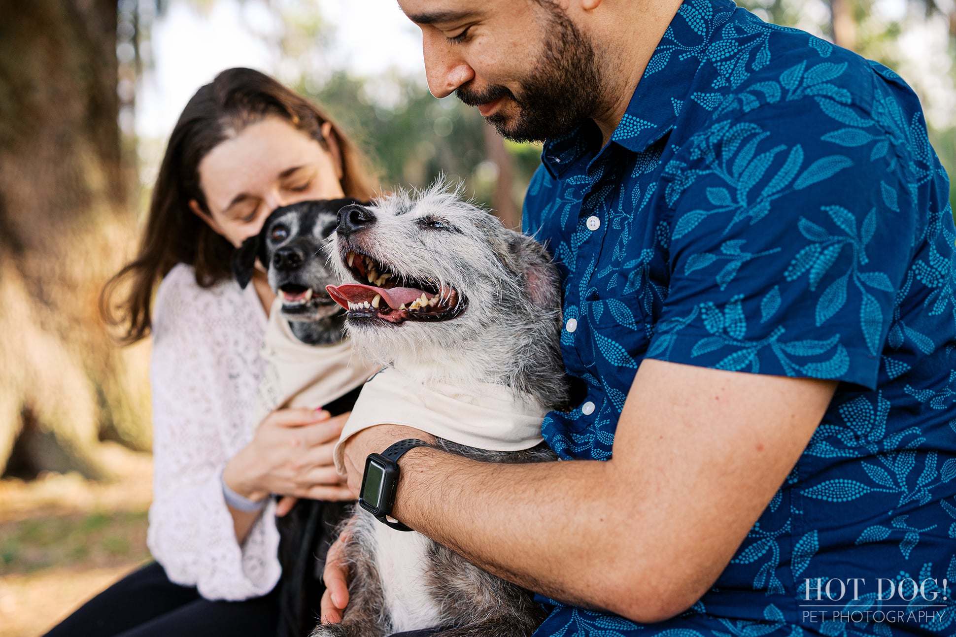 Juan cuddles Lana, a shaggy gray and white rescue dog, while Lauren holds Lila during their family pet photography session at Cypress Grove Park.