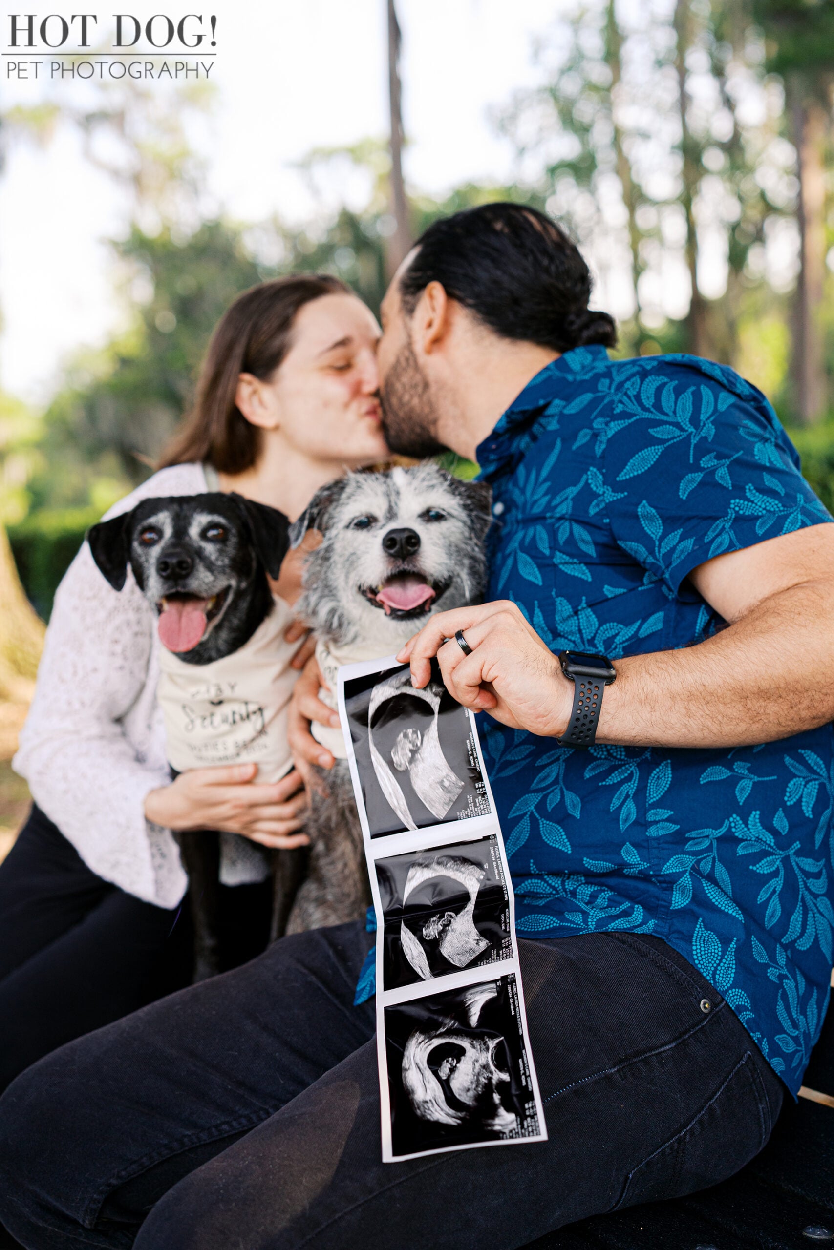 Lauren and Juan share a kiss while Lila and Lana sit between them wearing big sister bandanas, with ultrasound photos celebrating their pregnancy announcement.