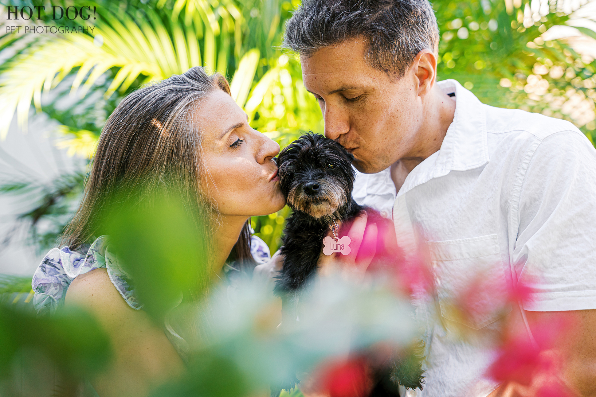 Luna getting a kiss from both her mom and dad surrounded by lush greenery.