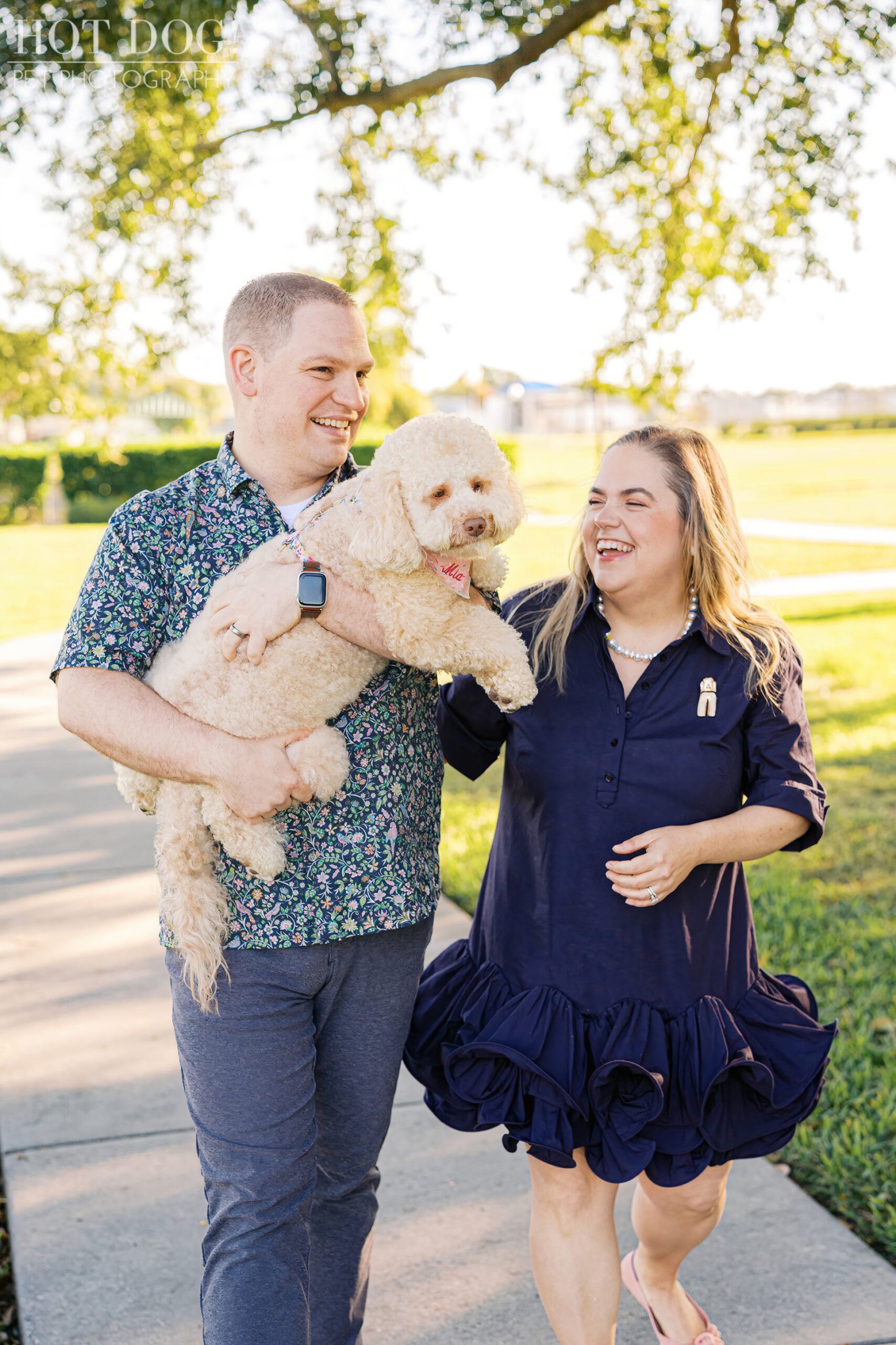 Ian holds Mia in his arms while walking beside Lauren, both smiling as they stroll together through Newton Park on a sunny morning.