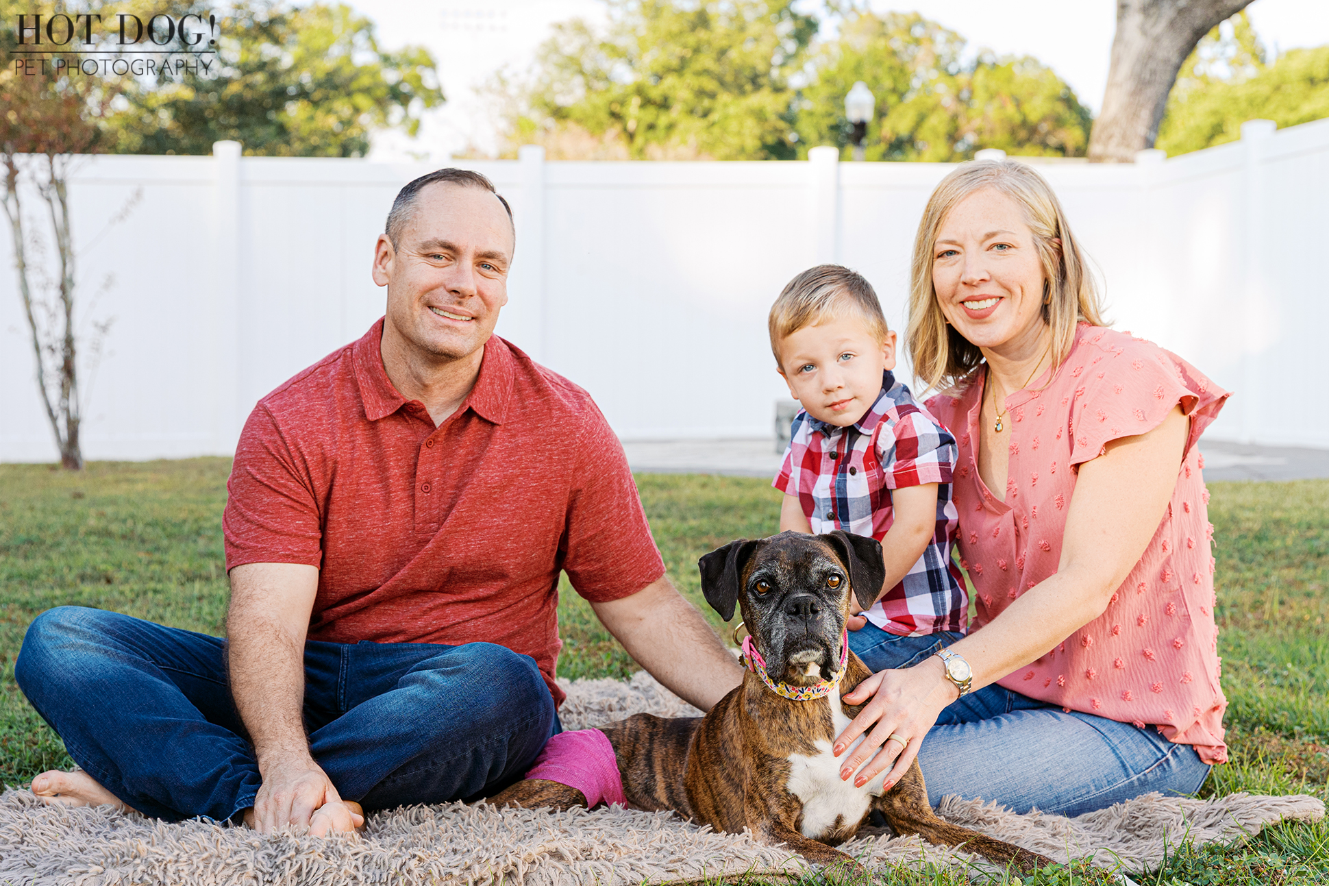 Family seated together outdoors with their senior brindle boxer centered in front of them, photographed during a calm backyard session.