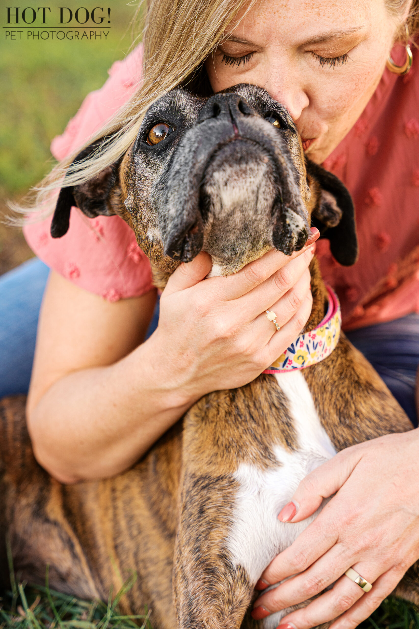 Mother kissing her senior Boxer gently on the head during an outdoor session.