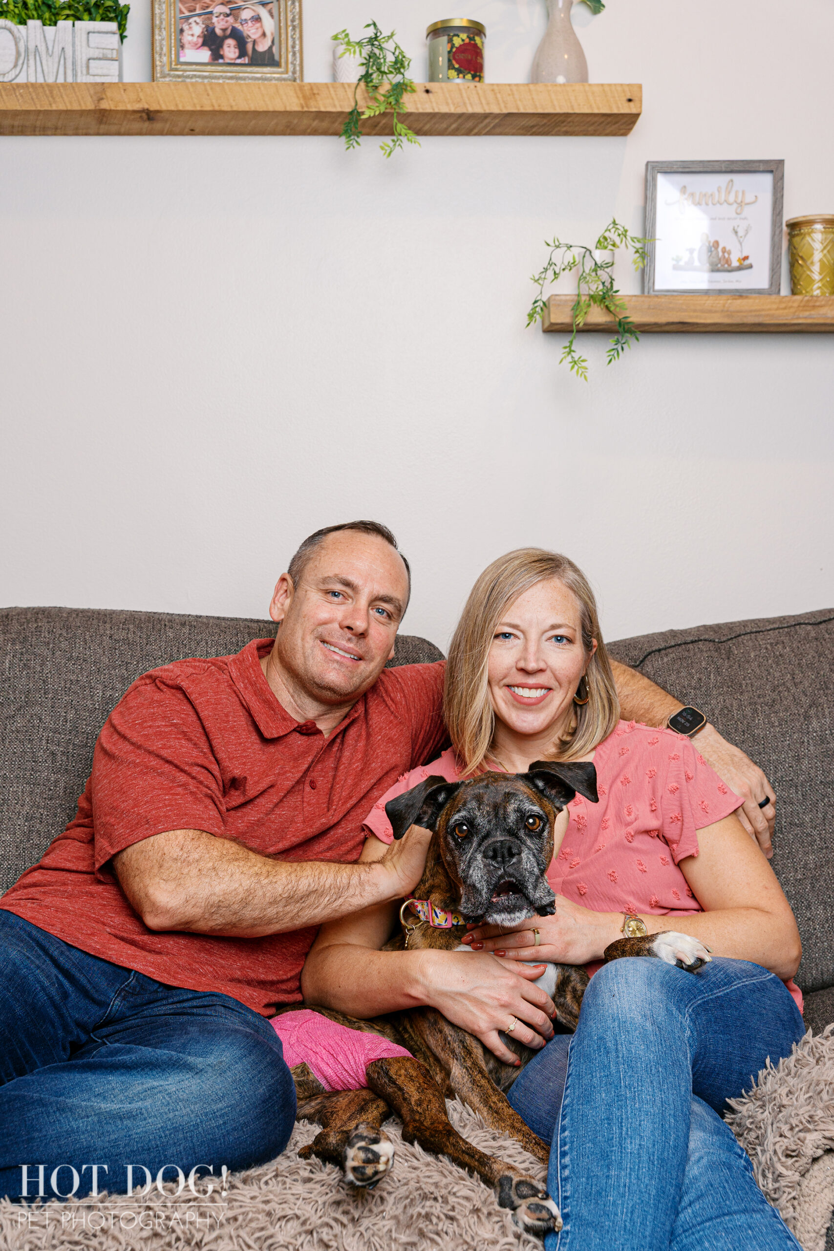 Family seated on a couch holding their senior Boxer close in an in-home session.