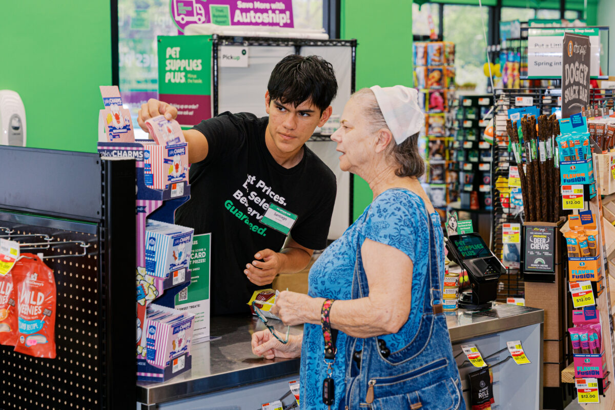 Employee assisting customer at pet store checkout with dog present, candid retail interaction photography.