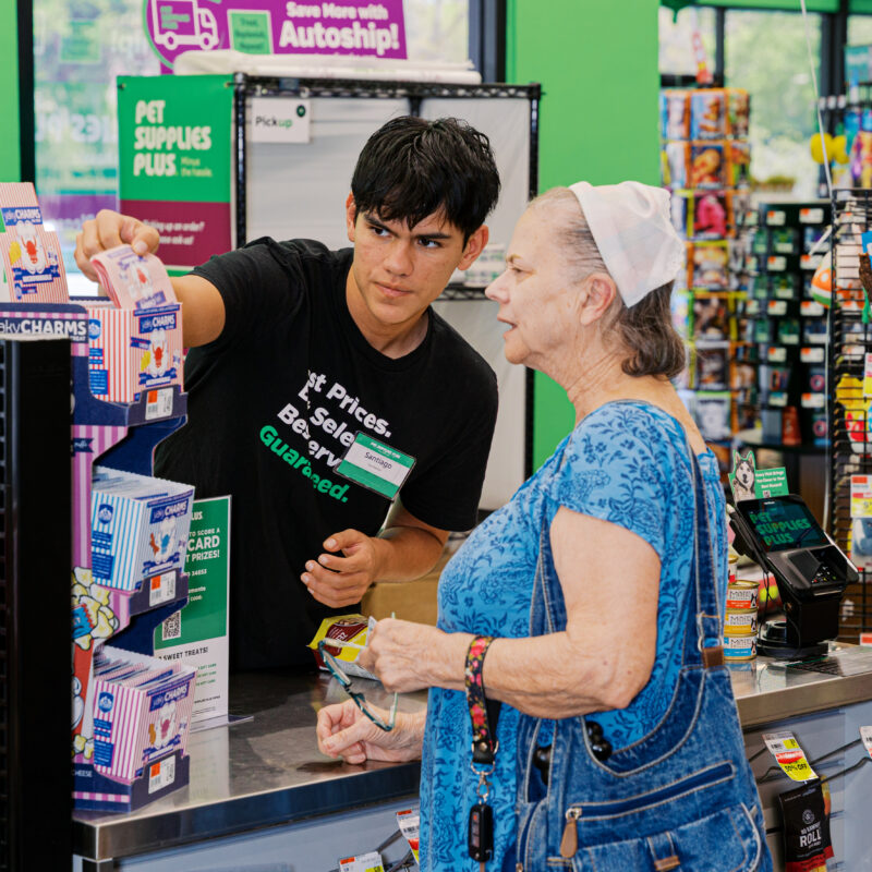Employee assisting customer at pet store checkout with dog present, candid retail interaction photography.
