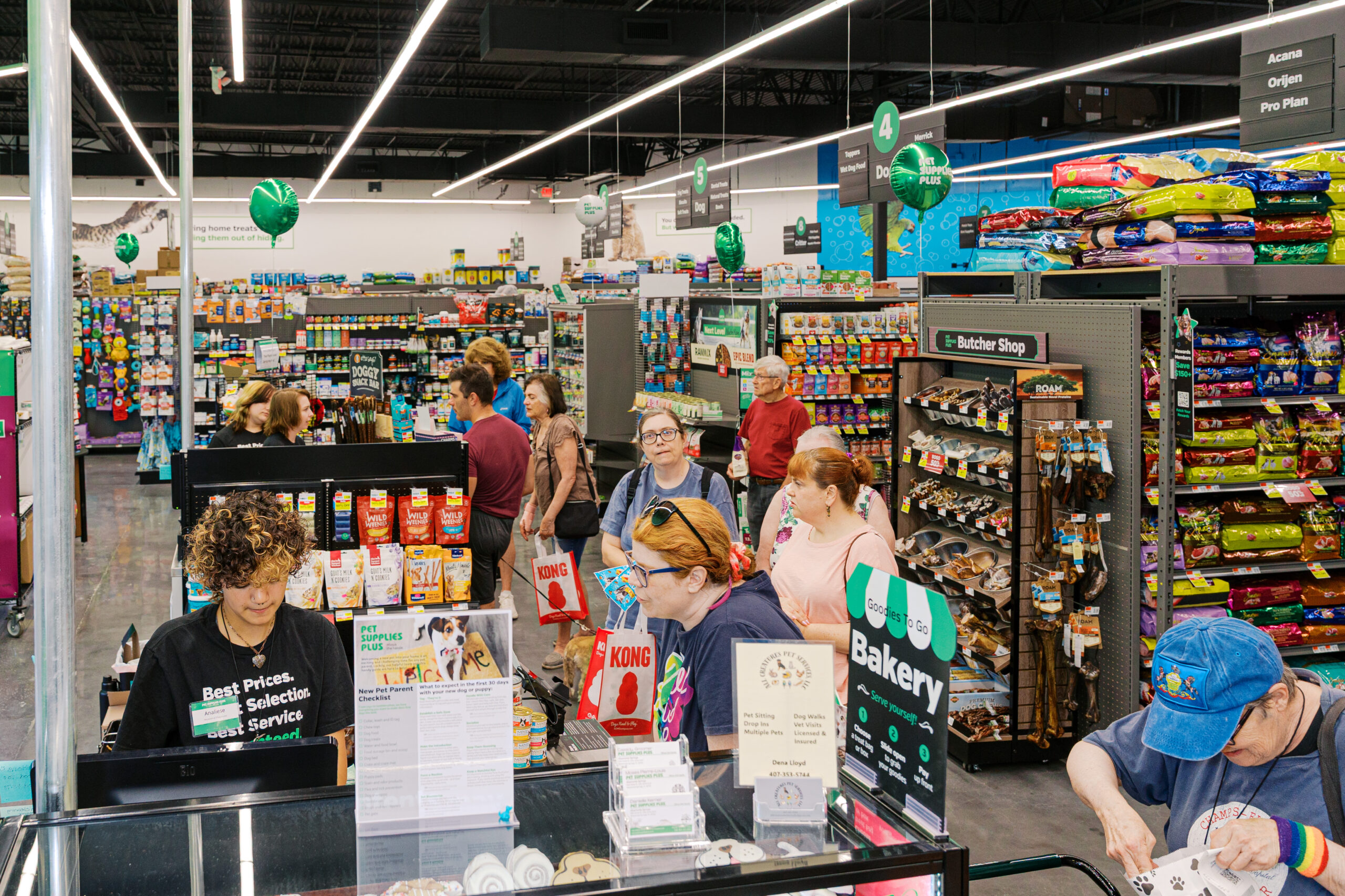 Busy pet store checkout area with customers and dogs, capturing high foot traffic during grand opening event.