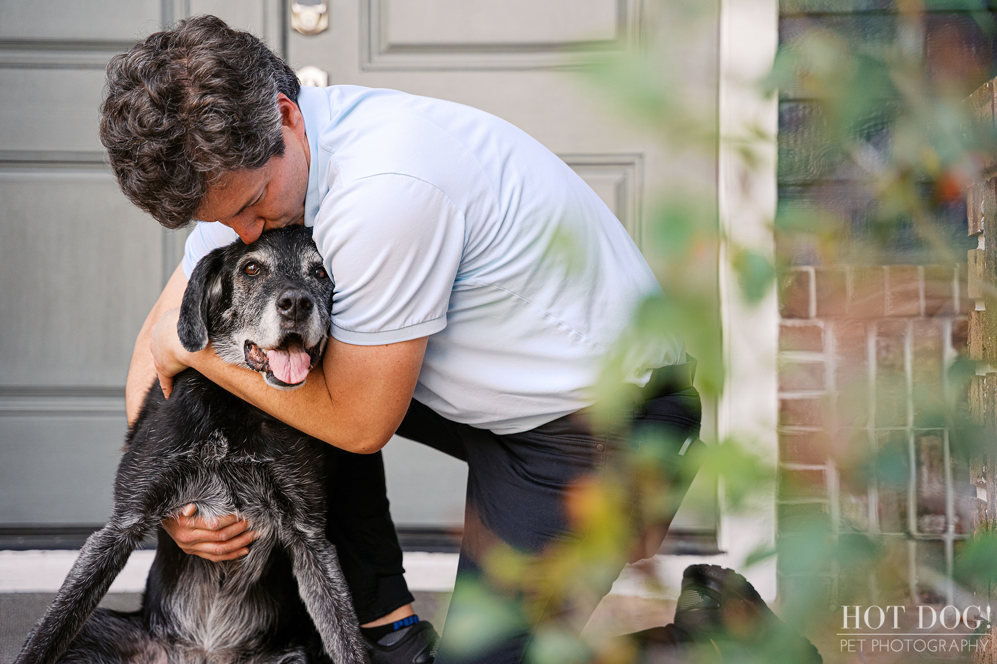 Senior black dog with a gray muzzle being gently hugged by her owner on the front porch during an at-home Lake Mary pet photography session.