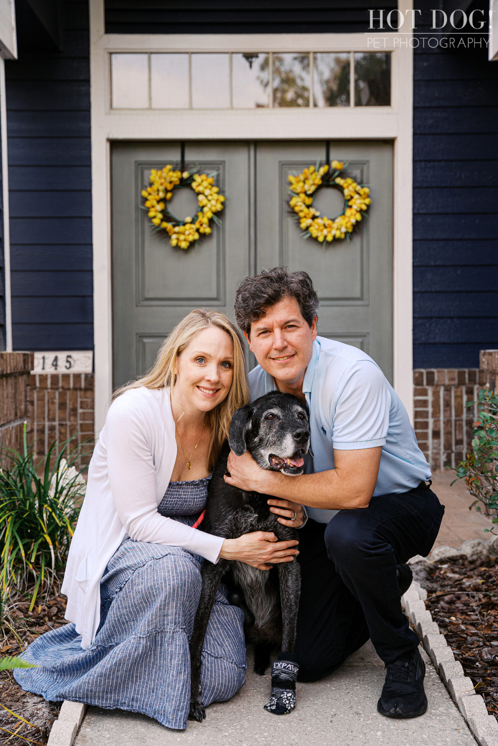 Lauren and Peter posing with Sadie in front of their Lake Mary home during a family pet photography session.
