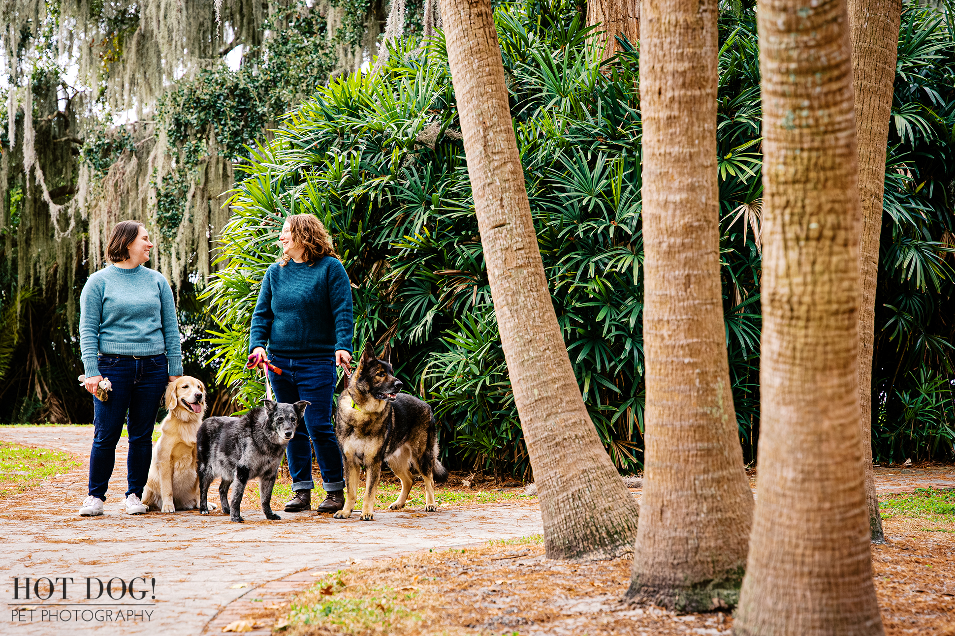 Lindsay and Aimee standing with their three dogs along a tree-lined path at Cypress Grove Park in Orlando, Florida.