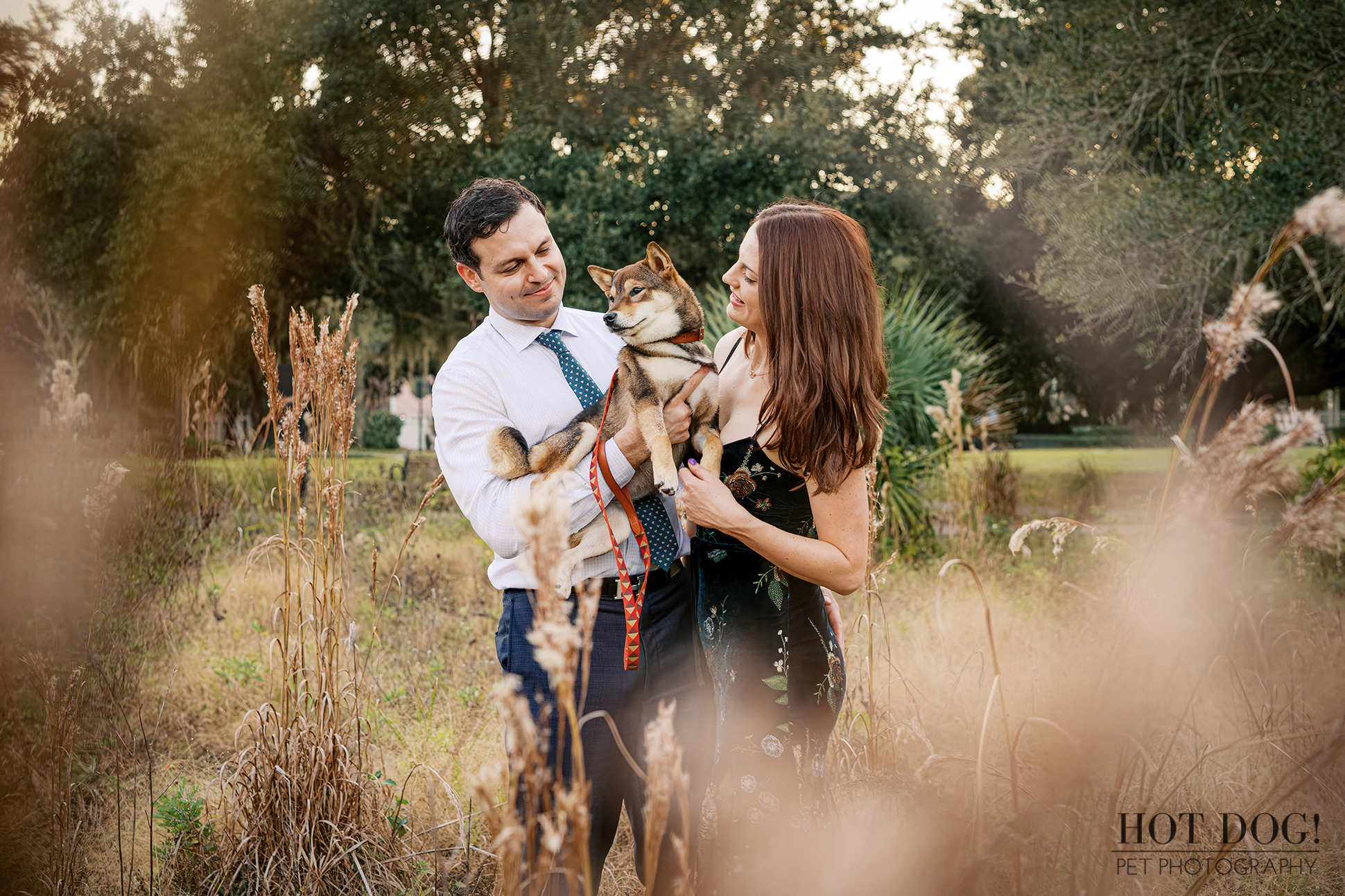 A happy young couple cuddles their Shiba Inu puppy in a field.