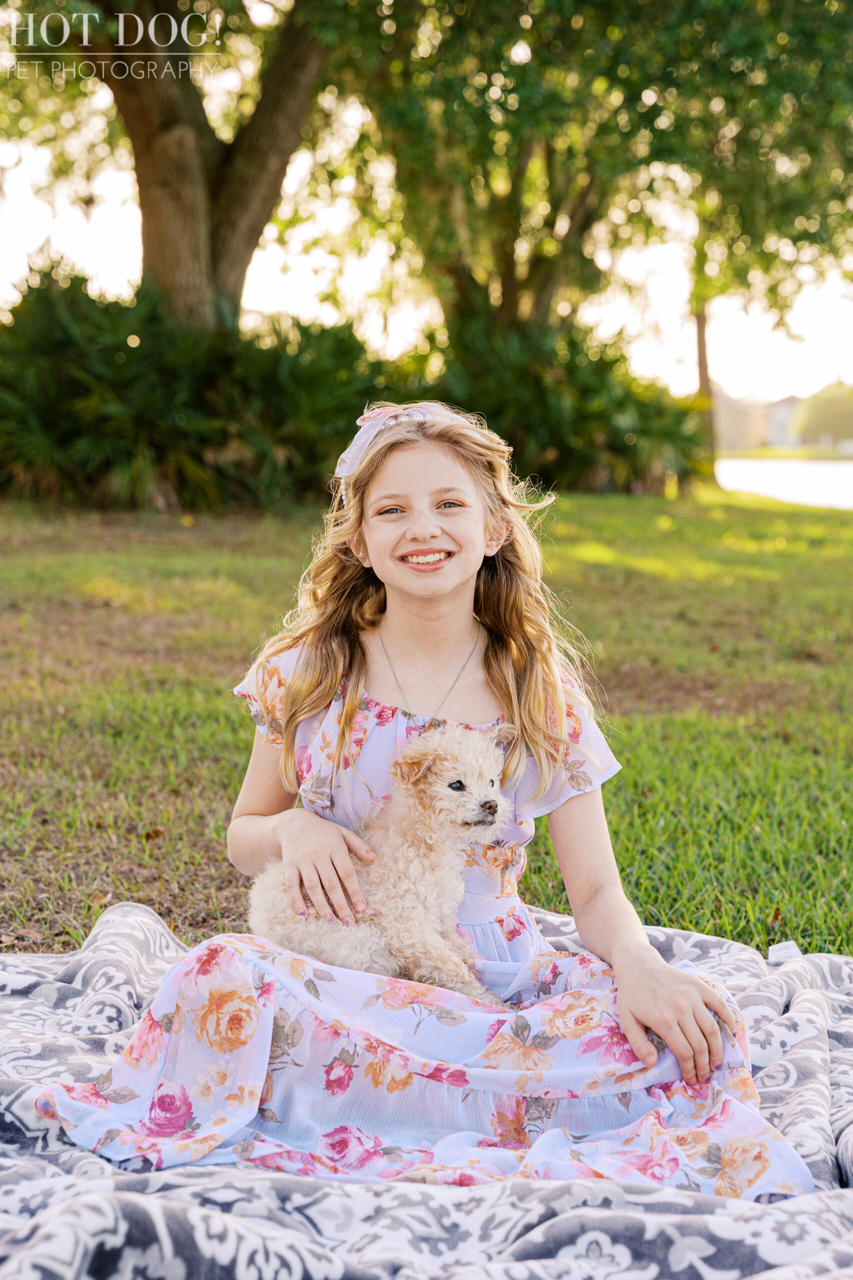 Young girl sitting on a blanket outdoors holding her senior Jack Russell Terrier during a sunset family pet photography session.