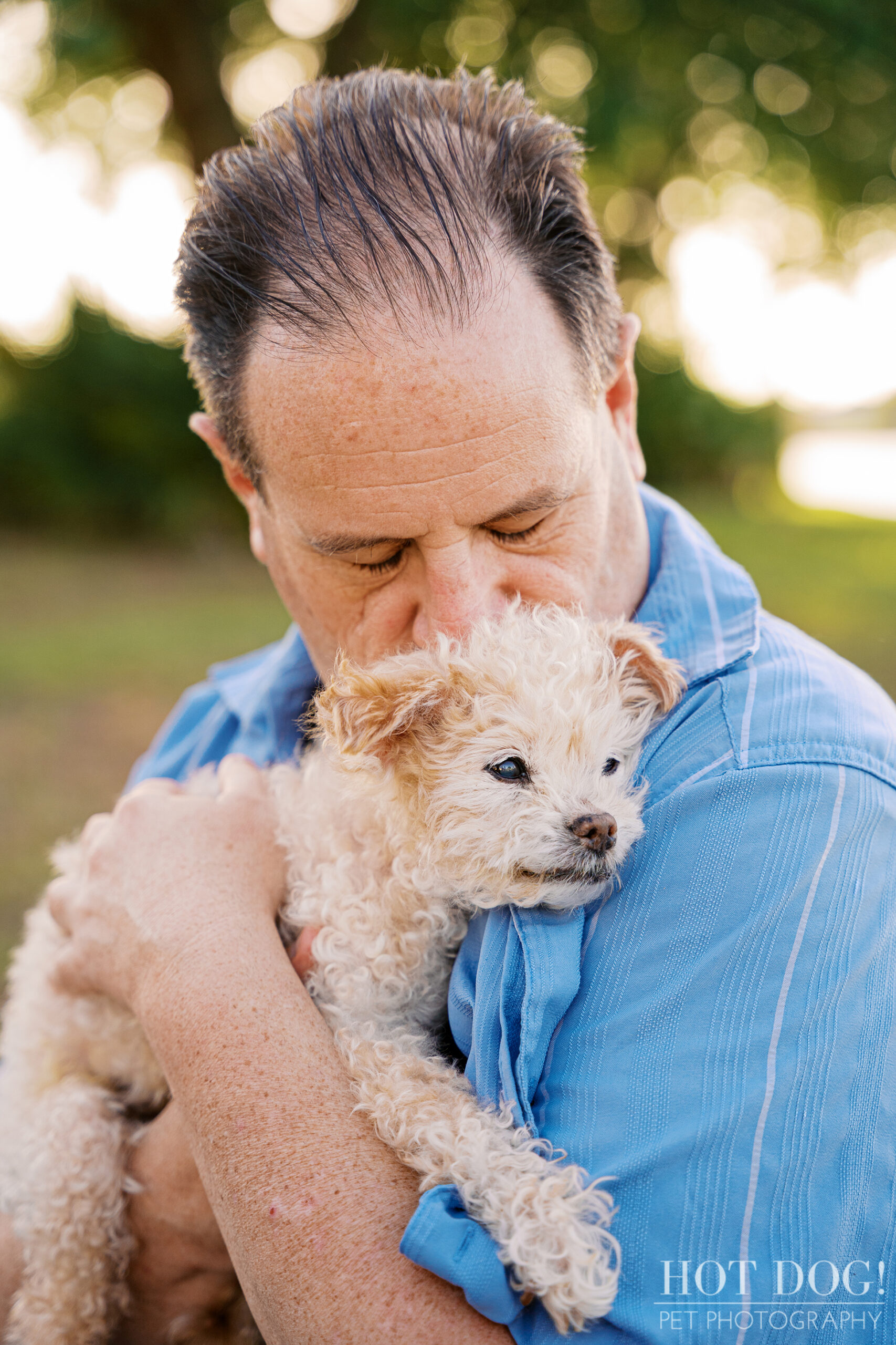 Father holding and kissing his elderly Jack Russell Terrier during a heartfelt outdoor cherished companion session.
