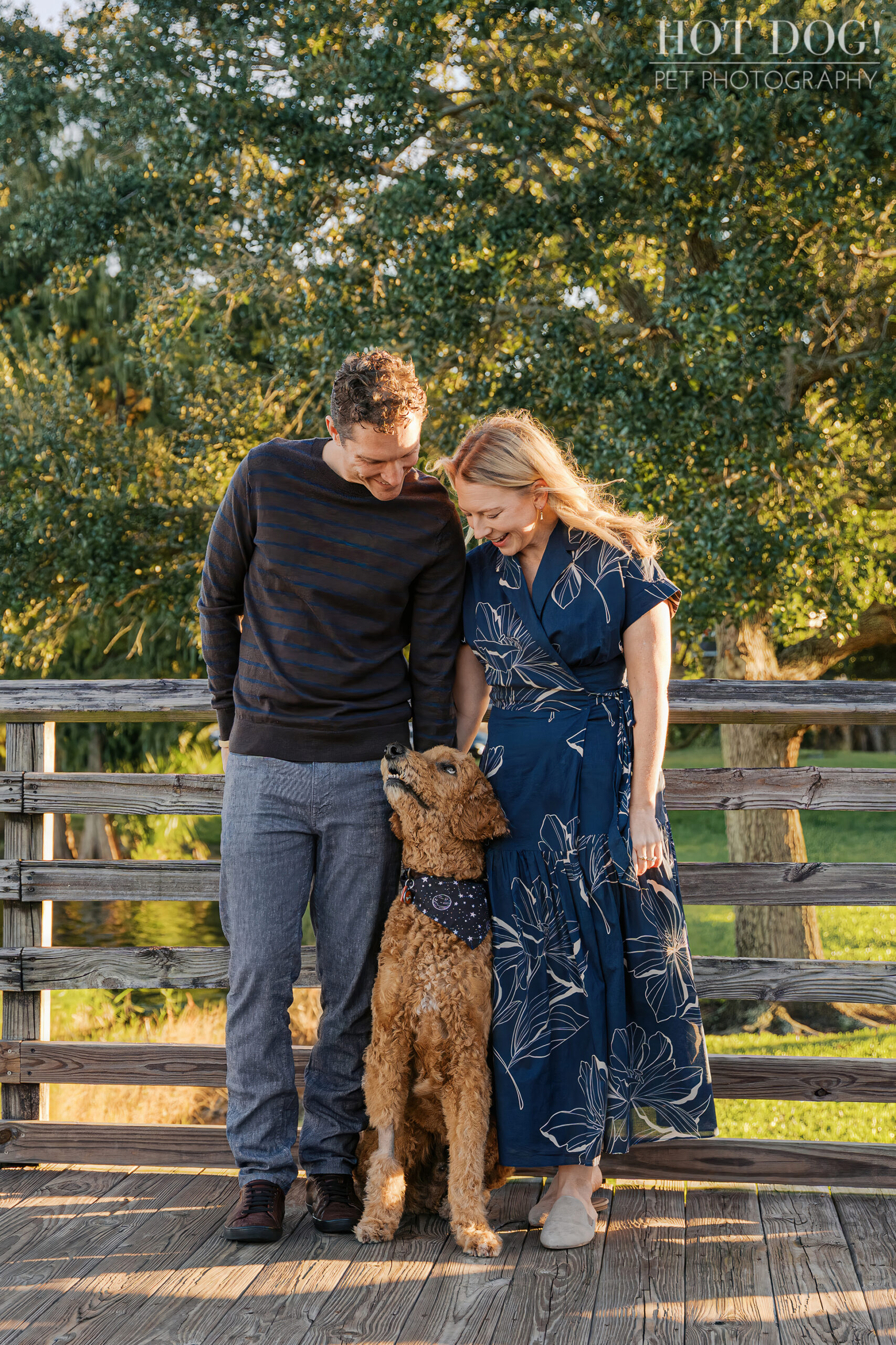 Jen and Cory standing on a wooden bridge, looking down lovingly at Wizard as he gazes up at them during their Cherished Companion Session.