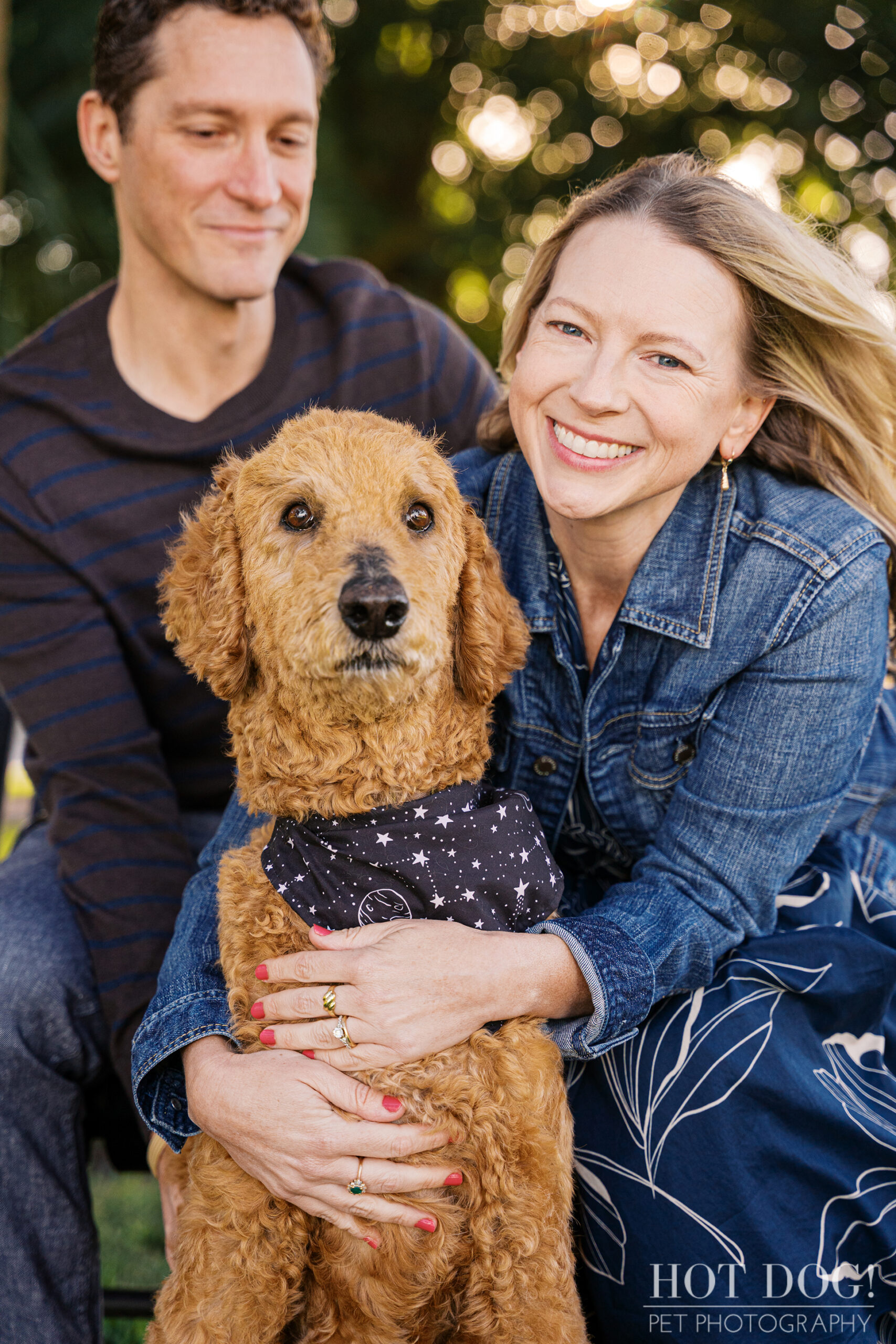 Jen smiling brightly while sitting beside Cory, gently holding Wizard close as he poses in his star-patterned bandana.
